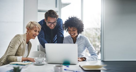 Drei Mitarbeitende arbeiten gemeinsam am Laptop und besprechen den Einsatz von KI im Unternehmen.