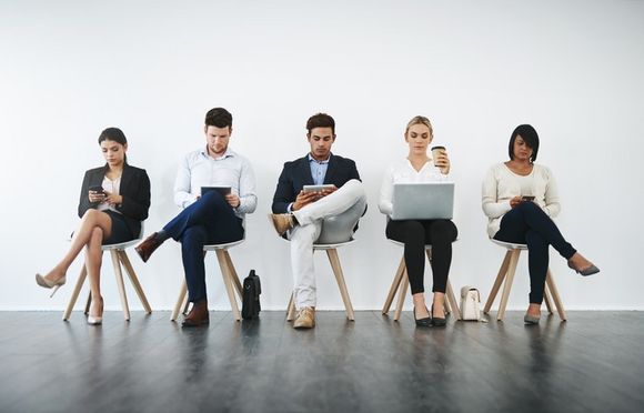 mehrere arbeitende Menschen sitzen wartend auf Stühlen