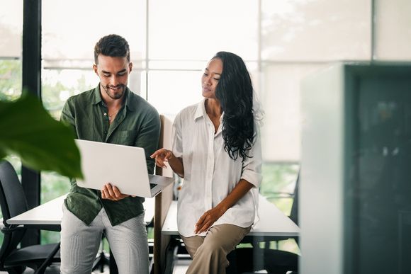 Mann und Frau schauen auf einen Laptop und arbeiten mit KI.