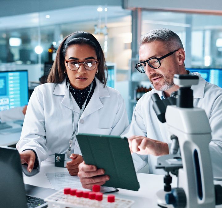 Zwei Fachkräfte im Healthcare-Labor analysieren Daten auf einem Tablet.