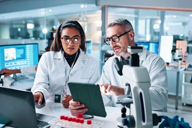 Zwei Fachkräfte im Healthcare-Labor analysieren Daten auf einem Tablet.